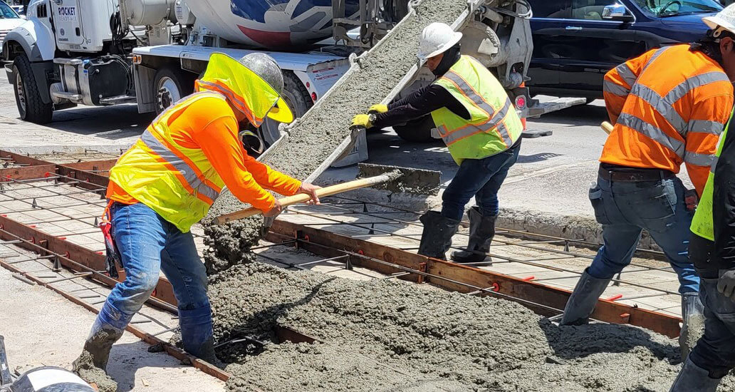 Construction workers filling area with concrete as mixing truck pours.